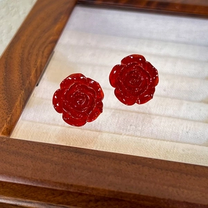 Detailed close-up of dark red rose earrings in a wooden vintage jewelry display box