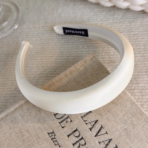 Detail of handmade cream satin sponge headband on textured book showing silk fabric texture