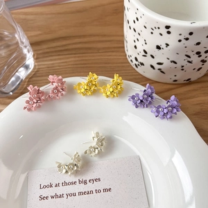 Detailed close-up of matte pastel flower earrings with pearls on a ceramic tray