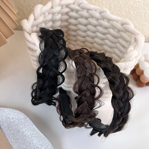 Three fishtail braided headbands in black, dark brown, and coffee on a woven basket
