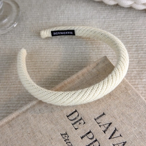 Close-up of beige knitted headband with a textured weave and a handmade woven label