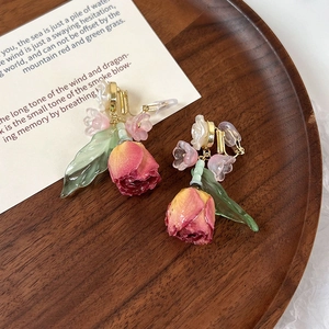 Detail van vintage clip-on oorbellen met gedroogde rode rozen en een groen blaadje