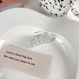 Close-up of small transparent rectangular hair claw clip with golden metal spring on ceramic tray