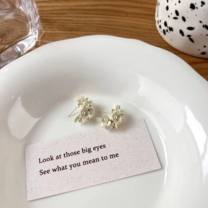 Detailed view of cream 3D flower earring with a pearl center on a white ceramic plate