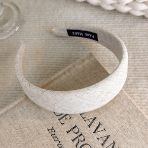 Close-up of a cream fabric headband with a black Hand Made label on its inner surface