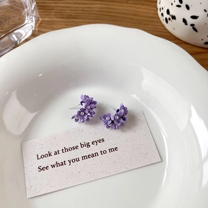 Detailed close-up of purple floral cluster earrings with small pearls on a ceramic plate