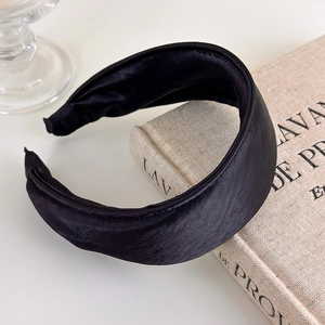 Detail of a padded black satin headband with silk luster placed on a vintage book