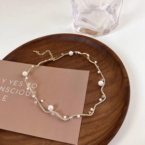 Detail of gold wavy chain necklace with pearls and floating rhinestones on clear fishing line