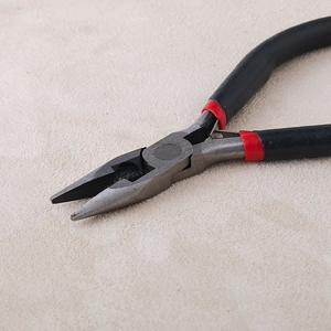 Gros plan détaillé sur une pince à bijoux avec poignées en caoutchouc noir et rouge