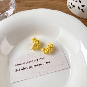 Close-up of yellow flower earrings with matte texture and small pearl center on white plate