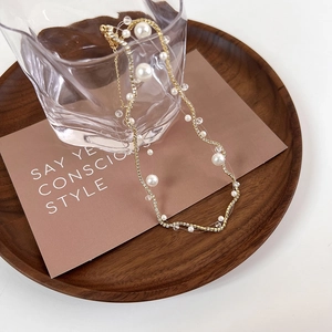 Detailed close-up of a gold pearl necklace with zircon accents on a rustic wood tray
