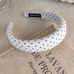 Detail of handmade cream headband with black polka dots on vintage book background