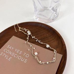 Detail of layered gold necklace featuring pearls and zircons on a rustic wooden tray