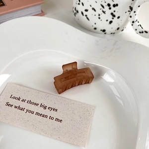 Macro detail of brown matte mini hair claw clip on an artistic ceramic white plate