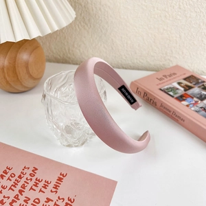Detail of pink padded sponge headband with handmade label on cream pleated lamp background