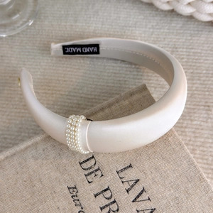 Detail view of cream-colored satin padded headband with pearl ring embellishment