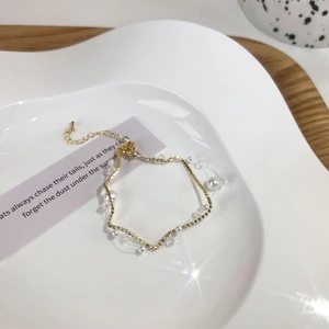 Detail of layered gold bracelet with white pearls and sparkling crystals on a ceramic tray