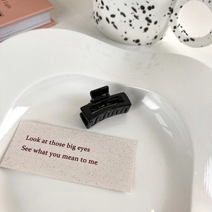 Glossy black rectangular hair claw clip displayed on a white ceramic heart-shaped plate