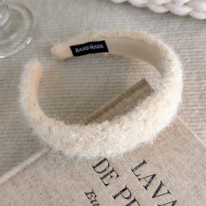 Close-up of beige plush headband with a handmade label on soft linen texture