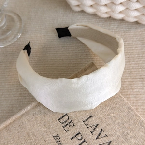 Close-up of beige satin wide pleated headband on vintage book showing fabric texture