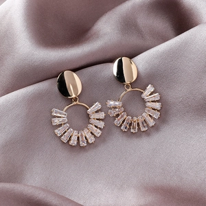 Elegant gold geometric earrings with oval crystal rings on purple satin background