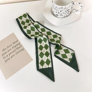 Detail shot of a green and cream diamond pattern satin skinny scarf on a white desk