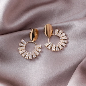 Detailed close-up of geometric gold earrings with rectangular crystals on silk fabric