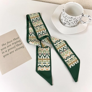 Detail of green silk twilly scarf with geometric patterns on a minimalist white table