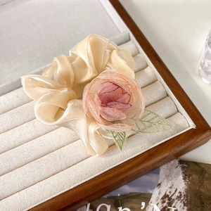 Detail van een organza scrunchie met roze stoffen roos en geborduurde groene bladeren