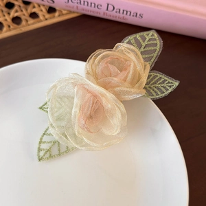 Detail van champagne roze organza camelia haarspeld met groen geborduurde bladeren
