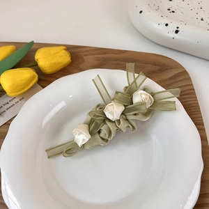 Detalle de pinza para el pelo verde menta con rosas de satén blanco en plato cerámico