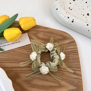 Detalle de coletero de satén verde crema con capullos de rosa blanca y lazos de organza
