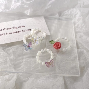 Gros plan de bagues en perles faites main avec rose rose et breloques papillon irisées