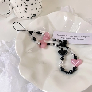 Handmade beaded phone strap with pink hearts, pearls, and black beads on a white tray