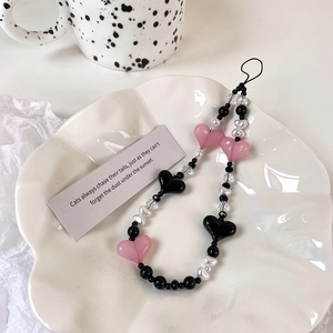 Detail of pink and black heart-shaped beaded phone strap on a white ceramic plate