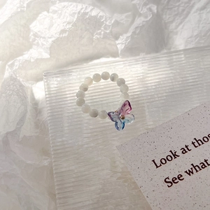 Détail d'une bague perlée avec breloque papillon dégradé sur support acrylique