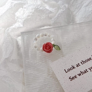 Détail de la bague perlée avec rose rose et feuille verte sur plateau en verre