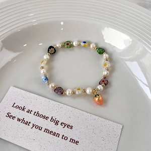 Détail du bracelet fait main avec perles d'eau douce et petit pendentif fraise rouge