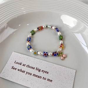 Détail d'un bracelet perlé avec perles d'eau douce, fleurs en verre et un pendentif cerise