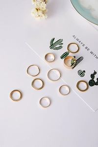 Close-up of 10-piece minimalist gold rings set on white surface with dry flowers