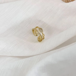 Détail d'une bague dorée double couche avec zircons et texture chaîne sur tissu blanc