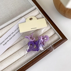Detail view of mini matte purple cross hair claws in OPP packaging on jewelry tray