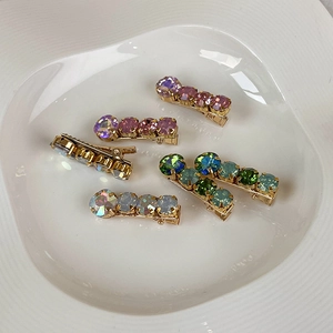 Close-up of golden hairpins with colorful rhinestones on a white ceramic plate
