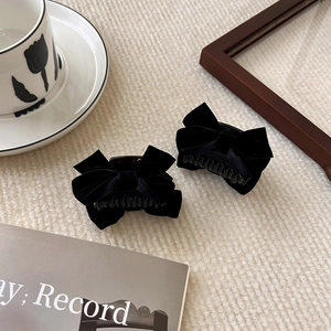 Pair of black velvet bow hair clips on a textured fabric background with vintage decor