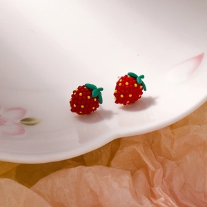 Close-up of strawberry stud earrings with green leaves on a white floral ceramic plate