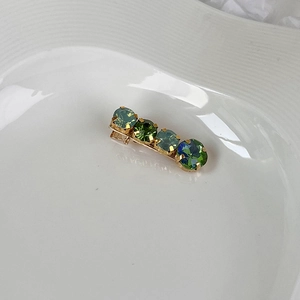 Detail of gold metal hair clip with four round gradient green and blue gemstones