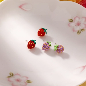 Detail shot of strawberry stud earrings in red and purple on a floral ceramic plate