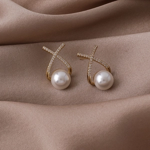 Détail de boucles d'oreilles perles dorées au design croisé serties de cristaux brillants