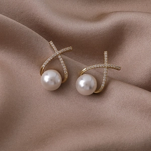 Détail de boucles d'oreilles dorées en X avec micro-pavé de diamants et perles blanches