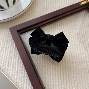 Detail of elegant black velvet bow hair claw clip on soft cream textured background